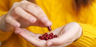 6 Expert-Recommended Vitamins and Minerals That Unlock Healthy Aging A close-up of a person picking a red vitamin out of a handful of red vitamins in their other hand while wearing a bright yellow sweater.