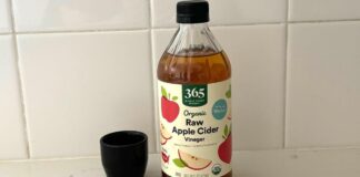 Here’s How to Harness the Power of Apple Cider Vinegar for Your Health A bottle of Whole Foods 365 raw apple cider vinegar next to a tiny black vase on a marble kitchen counter.