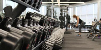Giant Fitness Clubs Adding Health Hubs an image of a weight rack at a gym with a woman standing at the end lifting weights