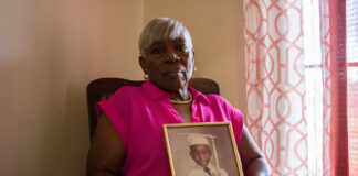 There’s a mental health crisis in Louisiana jails – The Current A woman wearing a pink shirt sits by a window holding a gold-framed portrait of a boy wearing a graduation cap and gown.