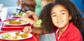 More Families Purchased School Meals After Federal Nutrition Policies Enacted Child with dark curly hair and red shirt eats a school lunch.