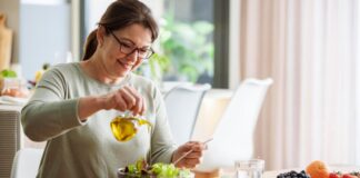2025’s Healthiest Diet: An Ultimate Guide to the Mediterranean Diet and Why It Works A woman with brown hair in a ponytail and glasses pouring olive oil onto a fresh salad.