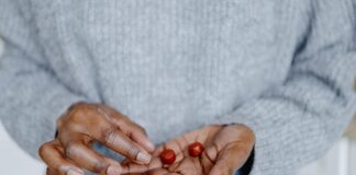 Mushroom Gummies: Side Effects, Benefits and Experts’ Cautions A close up of a person's hand holding two red gummy supplements. They are wearing a light grey sweater.