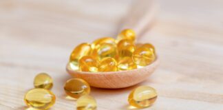 Vitamin E: Health Benefits, Nutritional Sources and Potential Drawbacks Vitamin D supplements on a wooden spoon, some have spilled onto the table.
