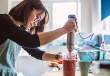 Being Consistent With 12 Simple Healthy Habits Can Transform Your 2026 Woman makes a fruit smoothie with an immersion blender.