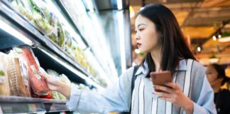 How AI Nutrition Information Could Help With Your Grocery Shopping A photo of a woman in a grocery store, looking at foods and her phone