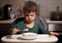 Specific foods linked to autism risk via immune pathways Young boy eats porridge from a spoon in a high chair