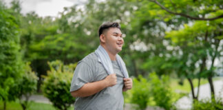 Walmart Launches Better Care Services and Rolls Back Prices on 1,000+ Wellness Essentials A smiling man is seen walking outdoors in a lush green park setting. He is wearing a gray shirt and has a towel draped around his neck. The background features trees and a pathway, creating a serene and natural environment.