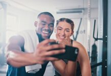 Can social media help you reach your health goals? Man and woman in the gym, taking a selfie on a phone camera