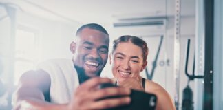 Can social media help you reach your health goals? Man and woman in the gym, taking a selfie on a phone camera