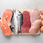 Boy Kibble Be Gone: April Davis Talks Latest TikTok Diet Trends for Reporting Texas | Elson S. Floyd College of Medicine News A wooden cutting board displays a variety of protein-rich foods, including salmon fillets, two whole fish, raw red meat, and raw chicken breasts and a dozen brown eggs.